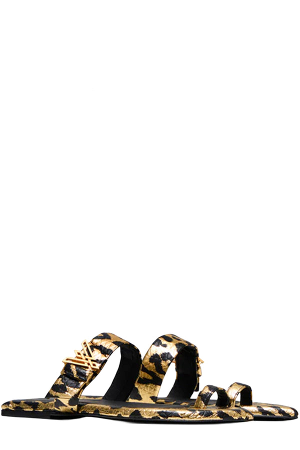 Rotated view of a pair of Vanda Novak flat sandals in gold and black with a golden logo made from leather, shown against plaid white background.