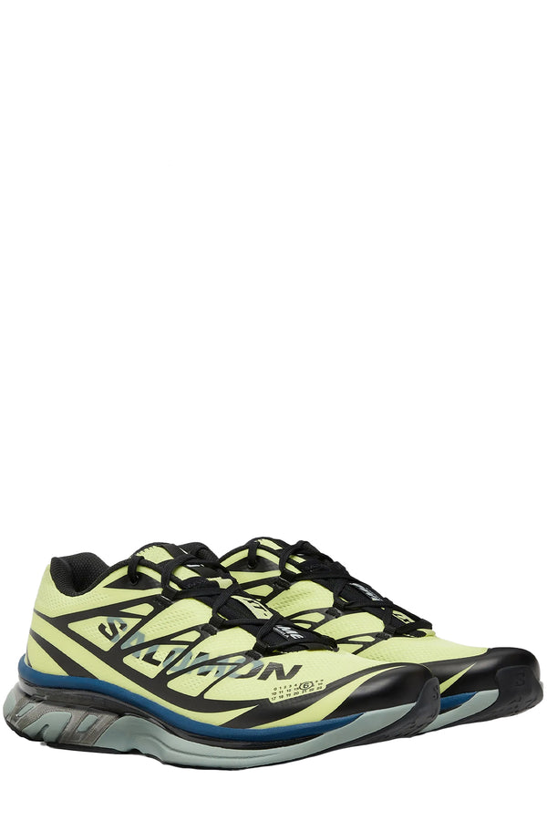 Rotated view of a pair of MM6 Maison Margiela sneakers in pale yellow, black, grey with a touch of dark blue, shown against a plain white background.