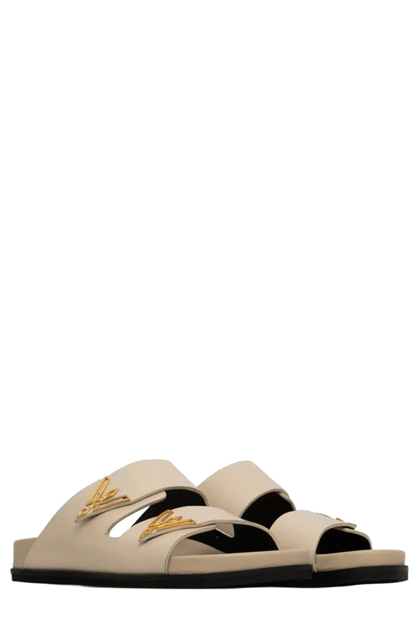Rotated view of a pair of Vanda Novak sandals in white made from leather with golden details, shown against plaid white background.
